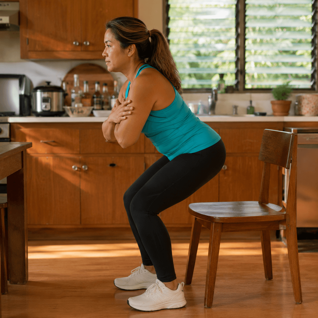 A local Filipino-Hawaiian woman in a turquoise top is mid-rise from a dining chair, arms crossed over her chest, halfway to standing.