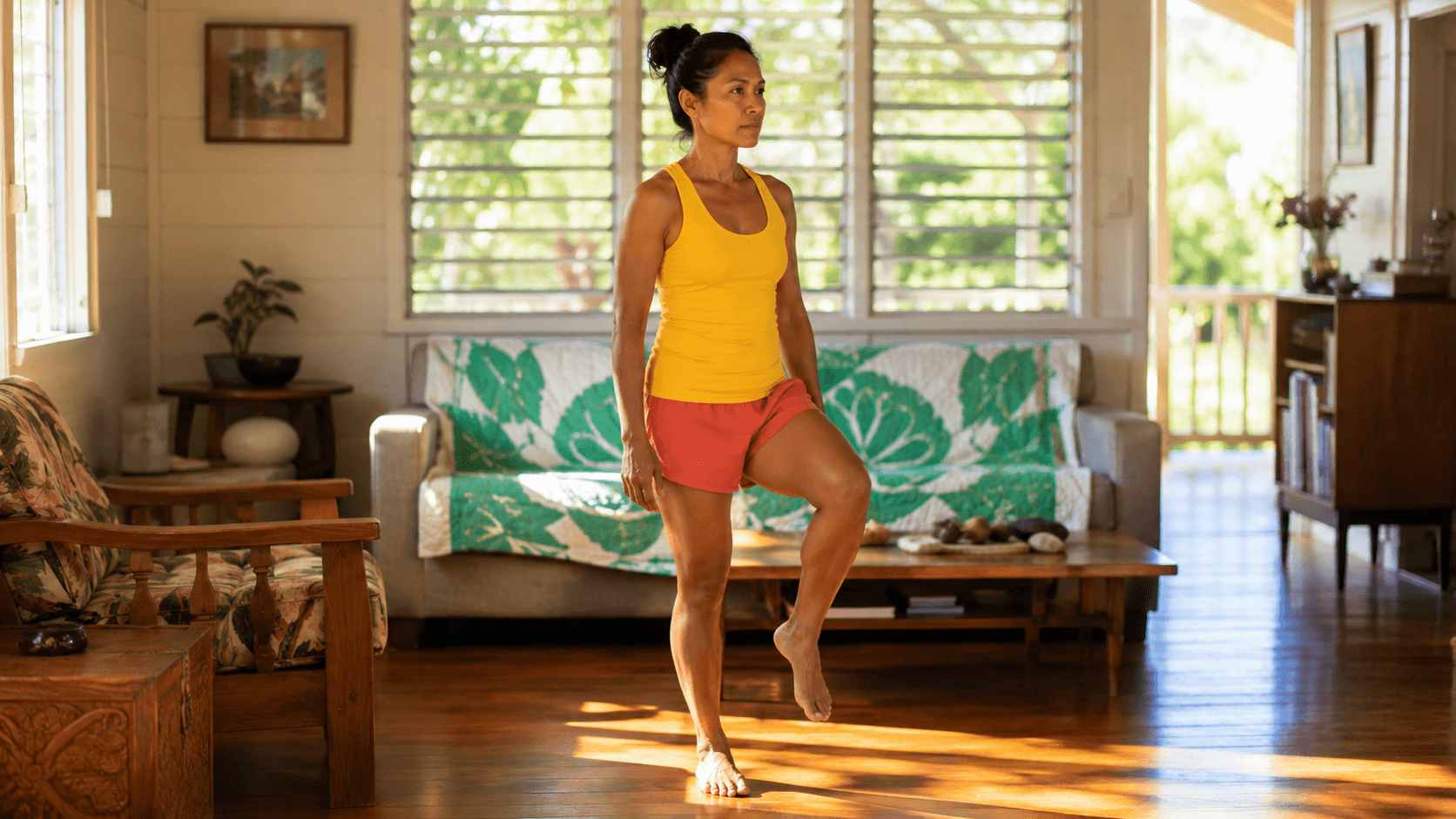 Woman in a yellow tank top standing on one leg in a Hawaiian living room with jalousie windows