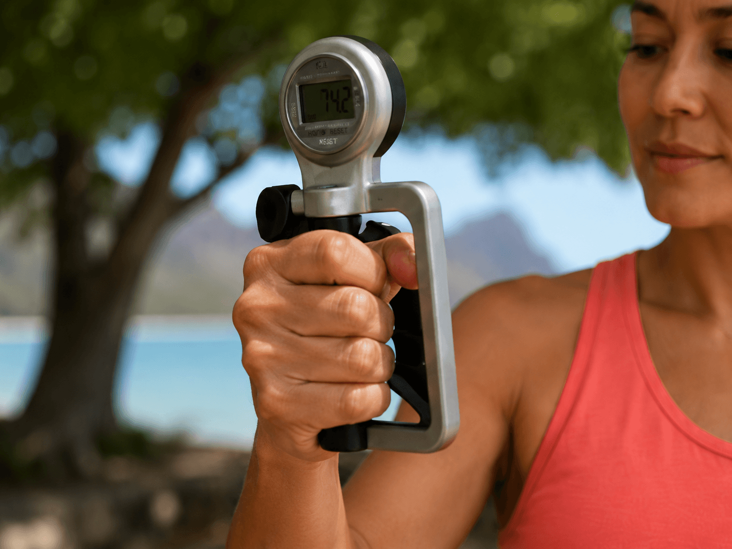 A close-up of a woman's hand squeezing a handheld dynamometer, with the strength reading visible on the display