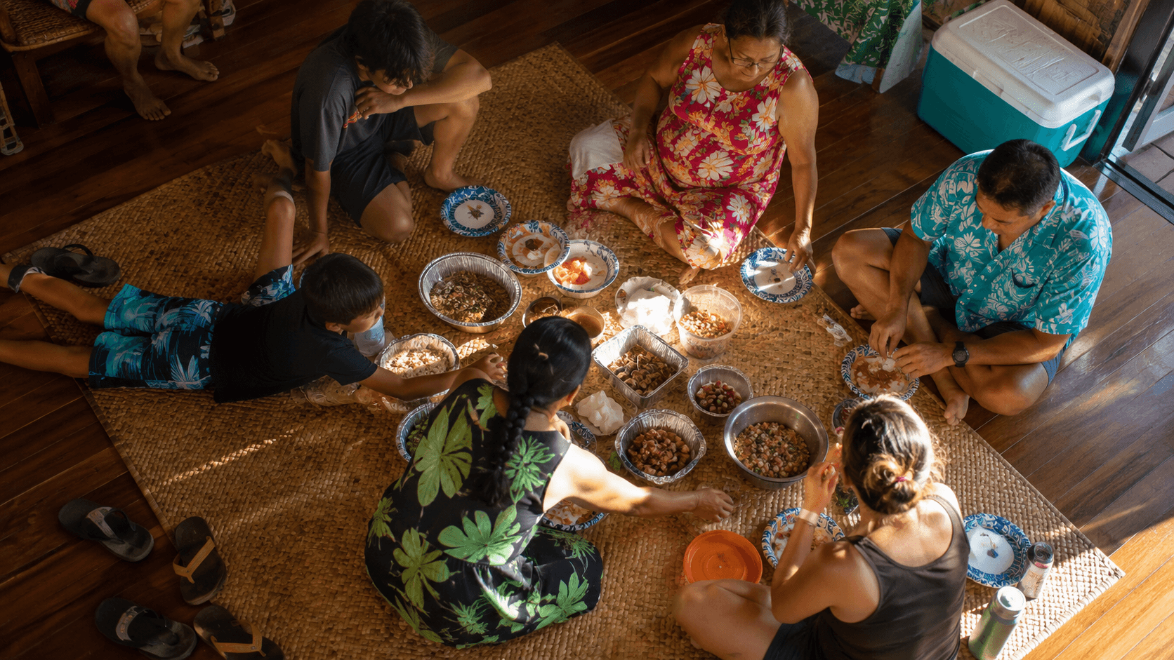 People of different ages sitting together on the floor around a shared meal